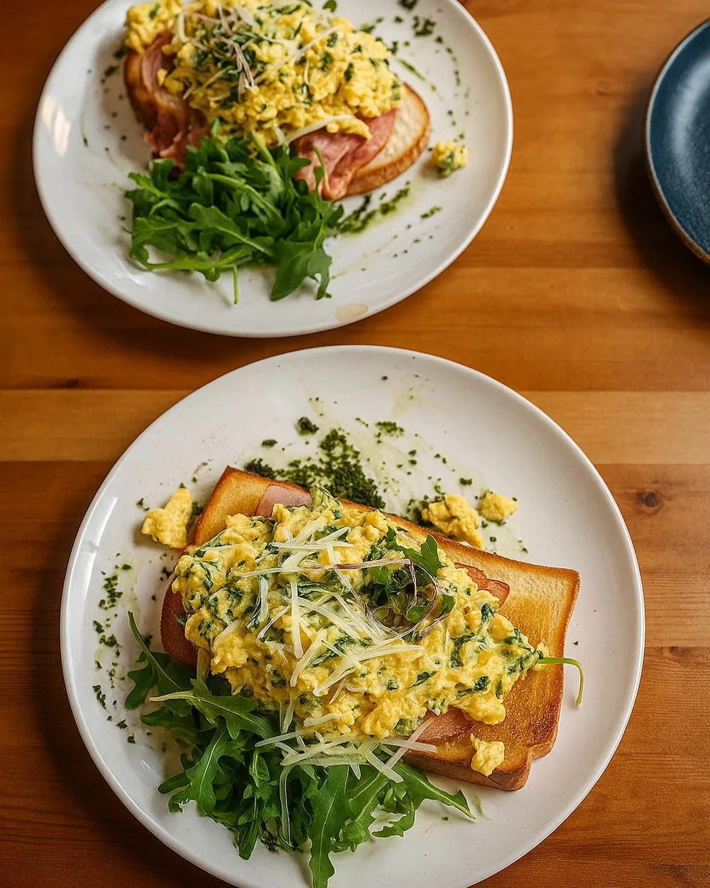 Two plates of scrambled green eggs on sourdough with rocket and shaved parmesan